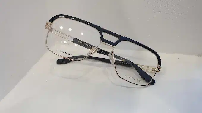 Lunettes Marc Jacobs noires et dorées sur surface blanche. Monture aviateur en acier inoxydable MJ 577 RHL 145.
