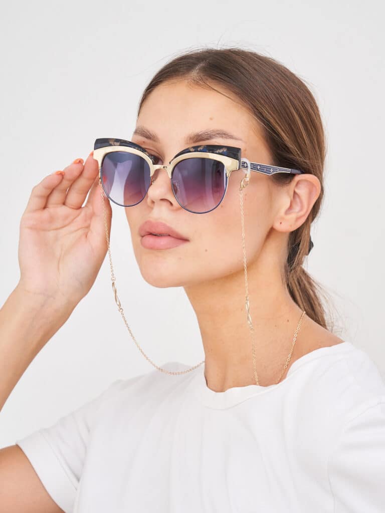 Femme élégante ajustant des lunettes de soleil cat-eye noires et dorées à verres dégradés, ornées d'une chaîne dorée chic.