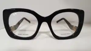 Lunettes de vue Marc Jacobs noires, forme œil-de-chat en acétate brillant. Détails dorés aux branches. Inscriptions : MARC JACOBS, ACETATE FRONT.