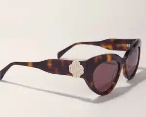 Lunettes de soleil œil de chat écaille de tortue marron. Un emblème argenté en forme de fleur orne la monture. Verres teintés foncés.